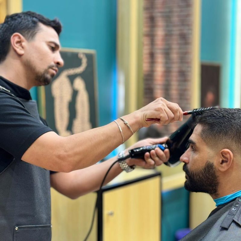 A barber brushing out a cut and lifting the hair with a dryer at the Dubai branch.
