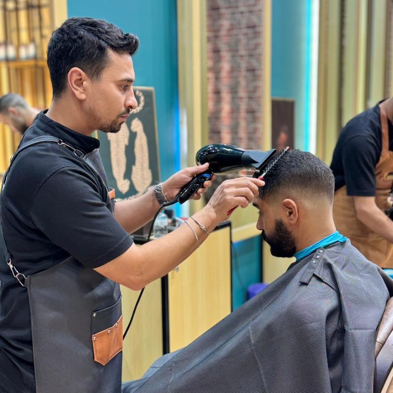 A barber drying and finishing a fresh cut with a spray bottle and towel, mid-service in the Dubai shop.