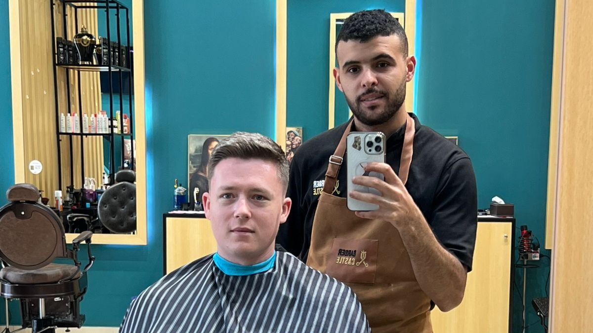 A client seated in the Castle chair with his barber standing behind him, the shop floor and the Google review sticker visible.