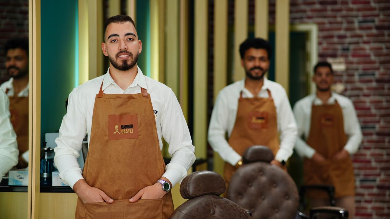 Barbers in tan aprons standing in the brass-partitioned salon